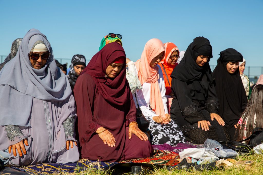 Women kneeling in prayer on blankets in the grass.